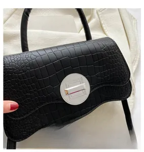 Détail du fermoir rotatif en métal argenté sur un sac noir à motif crocodile