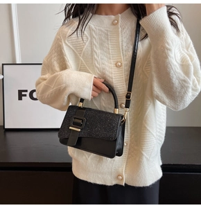 Détail du sac bandoulière pailleté noir avec boucle dorée sur un gilet blanc