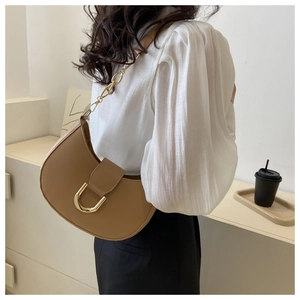 Gros plan d'un sac demi-lune marron clair avec boucle en U dorée et chaîne en métal