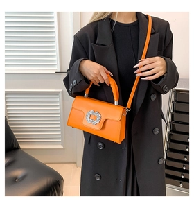 Detail of orange leather handbag featuring a sparkling crystal buckle and pleated handle
