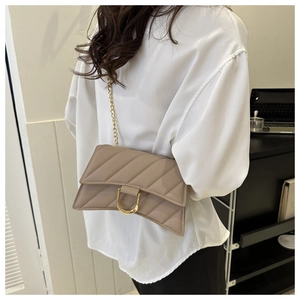 Detail of quilted leather crossbody bag with gold D-buckle and chain strap shown on model