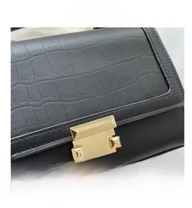 Detail of crocodile embossed leather texture and gold square buckle on black handbag