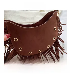 Close-up of brown suede crescent bag with hanging fringes and golden metal eyelets