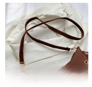 Detailed view of brown suede shoulder bag featuring fringe accents and gold buckle