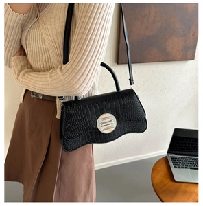 Détail d'un sac bandoulière noir effet crocodile avec un grand fermoir rond argenté