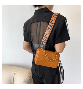 Detail of caramel quilted bag featuring amber acrylic chain and embroidered wide strap