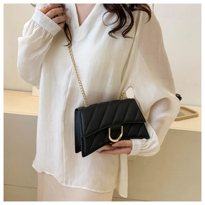 Close-up of black quilted crossbody bag with gold D-ring buckle and chain strap