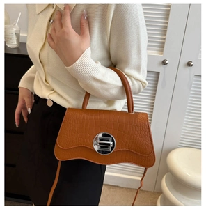 Détail d'un sac bandoulière marron texture crocodile avec fermoir rond argenté