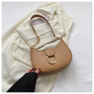 Détail du sac demi-lune camel avec boucle en D dorée sur fond de blazer blanc élégant