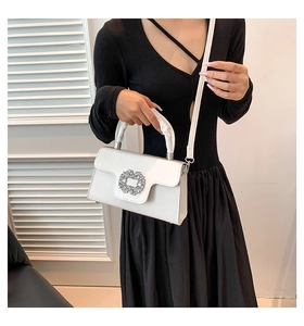 Close-up of a white leather bag featuring a sparkling crystal square buckle and ruched handle