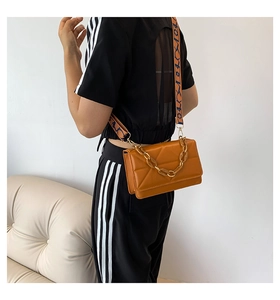 Detail of orange quilted crossbody bag with chunky chain and wide graphic shoulder strap