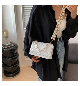 Close-up of white quilted crossbody bag with triangle texture and wide logo strap