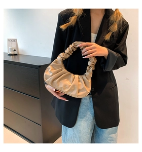 Detail of beige pleated cloud bag with soft ruched handle held by model in minimalist setting