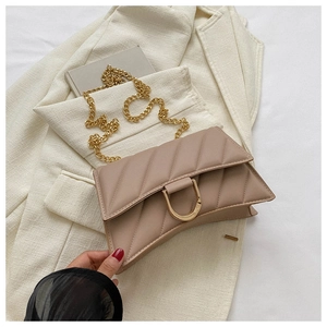 Detail of quilted beige chain bag with golden D-clasp on a light blazer background