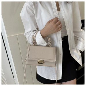 Detail of beige crocodile pattern handbag with knot handle and gold buckle