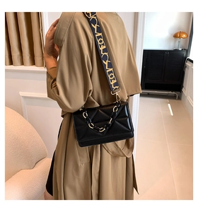 Detail of black quilted crossbody bag featuring resin chain and embroidered wide strap
