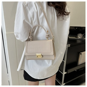 Detail of beige crocodile texture handbag with gold buckle shown on a model