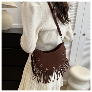 Detail view of dark brown tassel crescent bag in suede with golden eyelets on a model