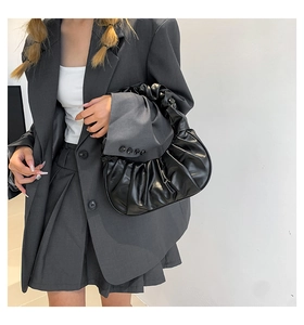 Detail of black ruched cloud bag made of glossy PU leather paired with grey blazer