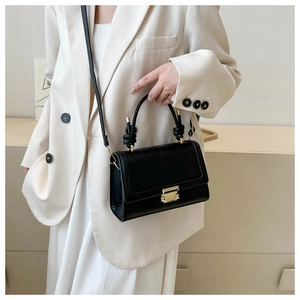 Model wearing black crocodile texture crossbody bag with gold clasp on white blazer