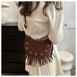 Detail of dark brown suede crescent bag featuring long tassels and gold metal eyelets