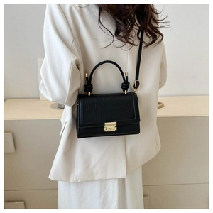 Detail of black crocodile texture pattern and gold clasp on a crossbody square bag