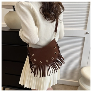 Close-up of brown suede tassel crossbody bag with metallic eyelets and bohemian fringe