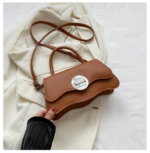 Détail d'un sac à main marron à motif crocodile avec base ondulée et fermoir rotatif argenté
