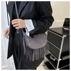 Detailed close-up of a grey suede crescent bag featuring long tassels and gold eyelets
