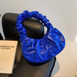Bright blue pleated cloud bag with scrunchie handle on a black leather chair