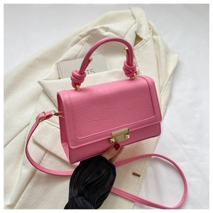 Detailed macro view of pink crocodile embossed handbag with golden buckle on a beige blazer