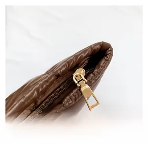 Close-up of smooth gold metal zipper and quilted puffer fabric texture on the brown bag