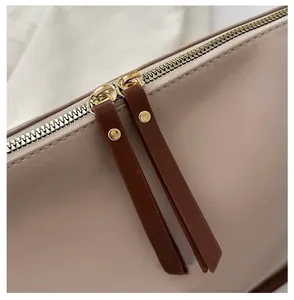 Macro view of gold metal dual zipper details with brown leather pullers on a tan bag