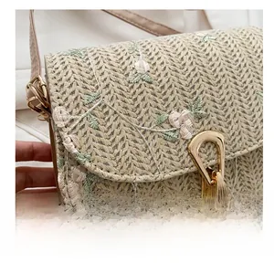 Detail of straw saddle bag featuring floral embroidery and gold metal buckle strap