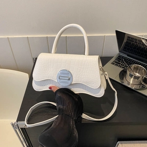 Sac bandoulière blanc effet crocodile avec fermoir argenté sur un bureau noir