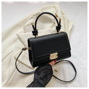Detail of black crocodile texture leather bag with gold buckle and knot handle decor
