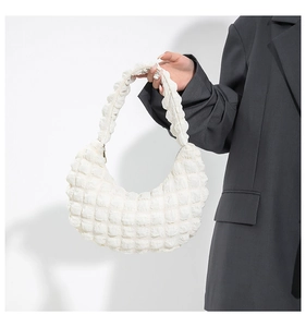 Detail view of white bubbly textured crescent bag held by a model in a grey suit