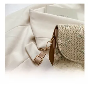 Macro shot of gold-tone metal hooks and delicate floral embroidery on straw bag