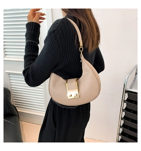 Detail view of a beige crescent underarm bag featuring a prominent gold buckle clasp