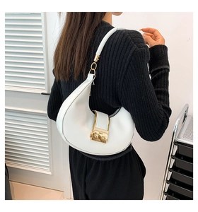 Detail of white leather hobo bag with gold buckle on shoulder of model in black top