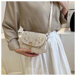 Detail showing floral embroidery and golden horseshoe lock on woven straw crossbody bag