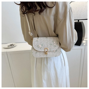 Detailed close-up of beige woven saddle bag with pink floral embroidery and gold buckle