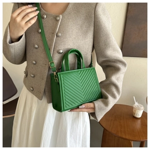 Detail view of bright green chevron-quilted handbag with gold-tone hardware on model