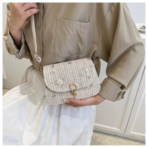 Detail of floral embroidery and golden horseshoe buckle on straw woven crossbody bag