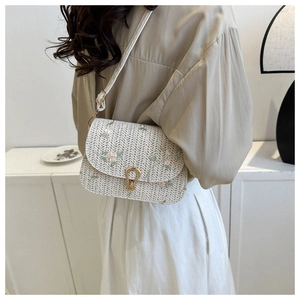 Detail of a beige woven straw saddle bag featuring delicate pink floral embroidery