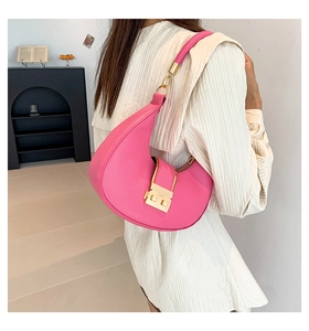 Rose pink crescent shoulder bag with gold clasp shown on a white pleated shirt background