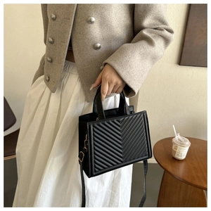 Detail of a black quilted tote bag with V-shaped stitching and adjustable shoulder strap