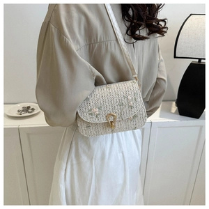 Detail of hand-woven straw crossbody bag featuring delicate floral embroidery and gold buckle
