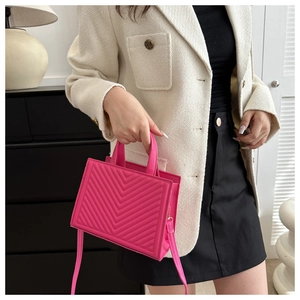 Detail of fuchsia quilted tote bag with V-shaped stitching held by fashion model