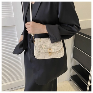 Detail of floral embroidery and gold horseshoe buckle on woven straw crossbody bag
